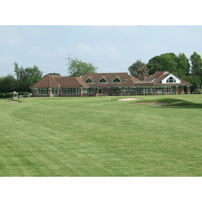 Spacious golf club building with large windows, surrounded by lush green grass and trees under a clear blue sky.