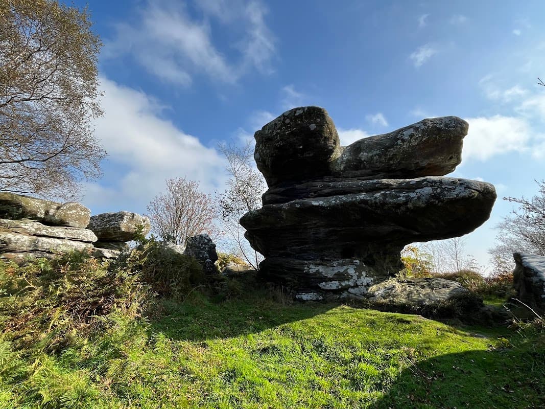 Unique rock formations surrounded by greenery under a partly cloudy sky at Brimham Rocks Car Park.
