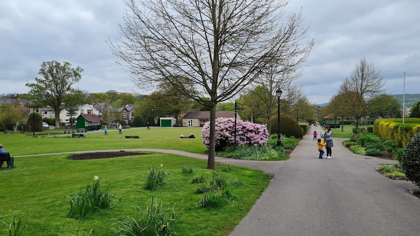 Lush green park with blooming trees, people playing bowls, and a path lined with shrubs in Sutton-in-Craven, Yorkshire.