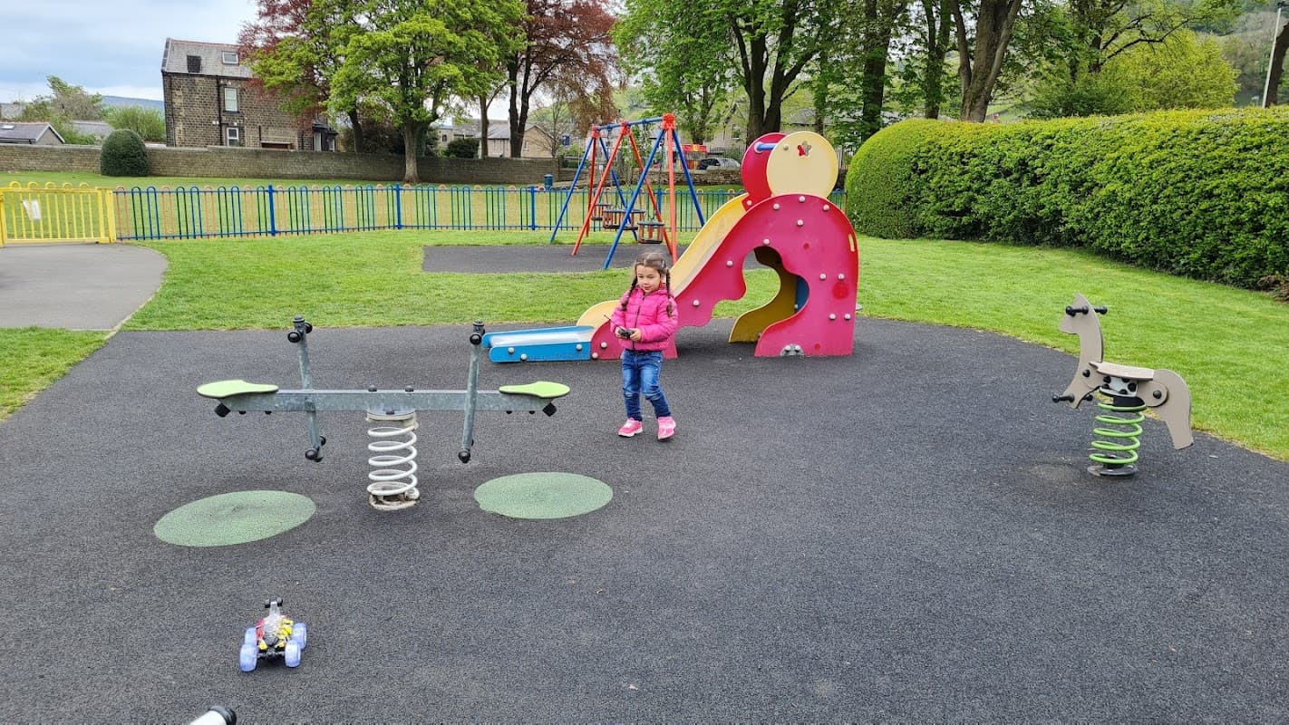 Colorful play area with a slide, spring animals, and a child playing on a spring seesaw surrounded by green grass.