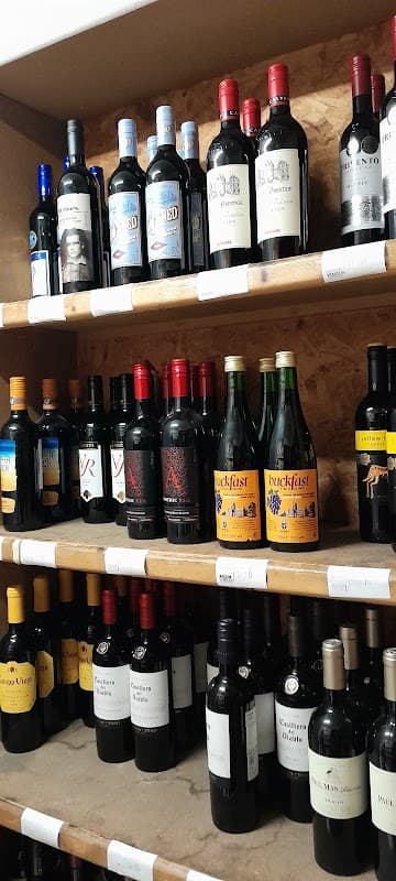 Shelves filled with various bottles of red wine, showcasing different labels and brands in a cozy corner shop.