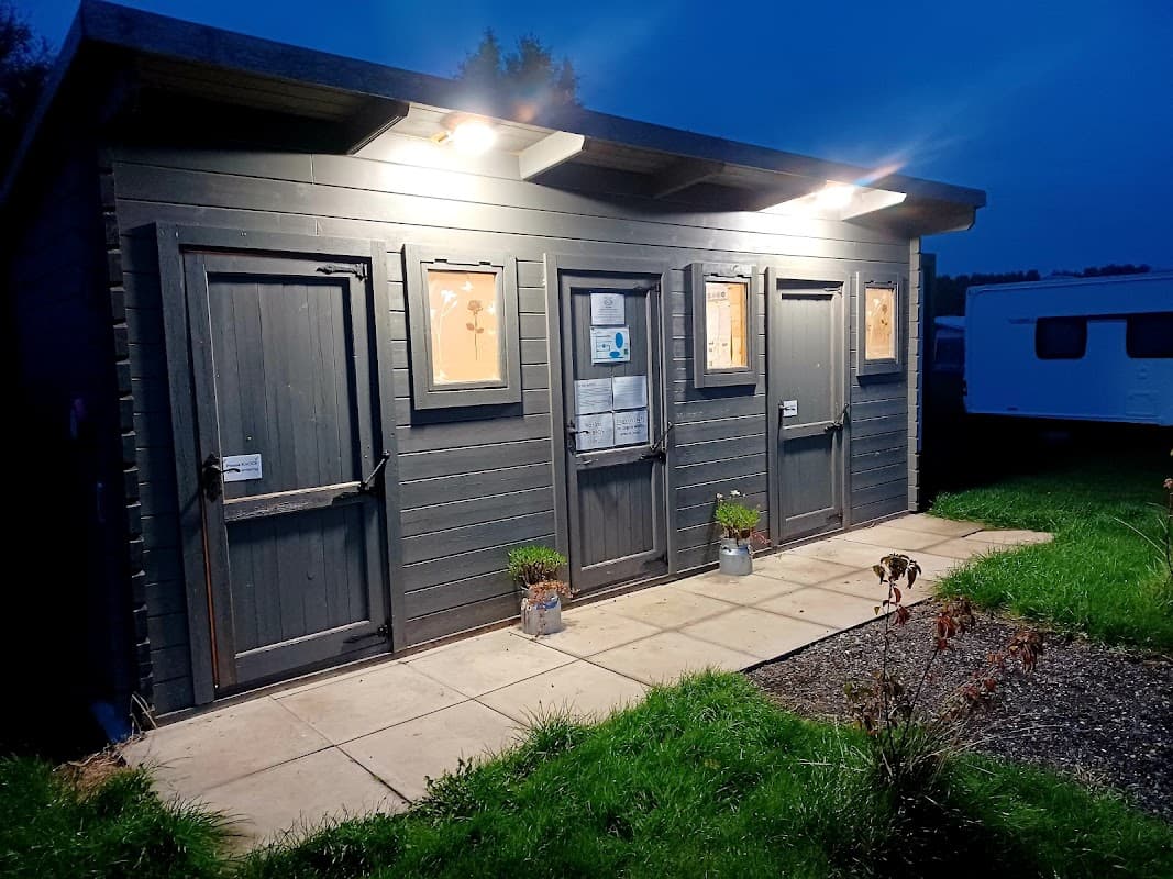 Three dark wooden doors with illuminated signage, set against a twilight sky, surrounded by grass and a gravel path.