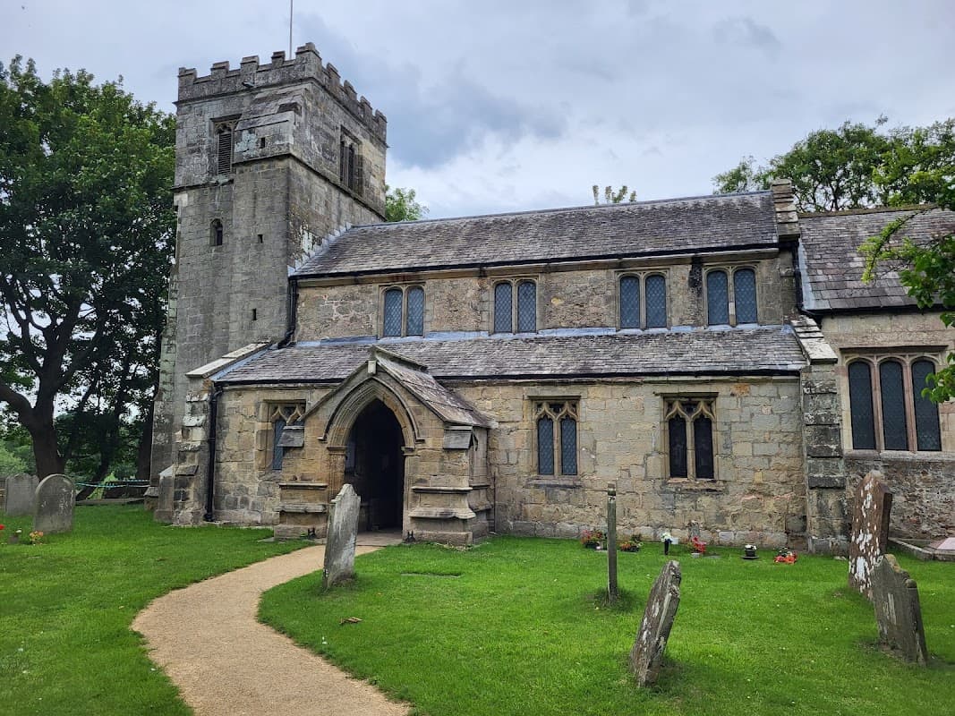 Historic stone church with a tower, arched entrance, and grave markers on a grassy path in Sutton upon Derwent, Yorkshire.