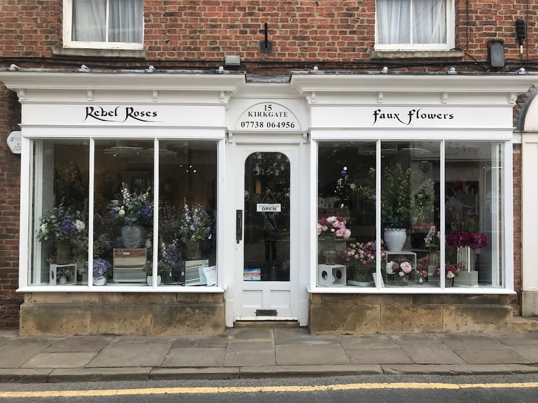 Shopfront of Rebel Roses, featuring large windows displaying colorful silk flowers and floral arrangements.