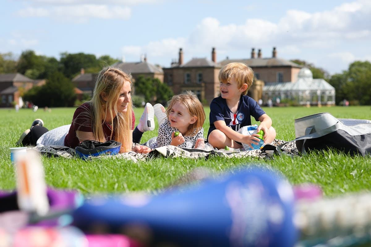 A woman and two children relax on a grassy field, enjoying a sunny day at Preston Park Museum & Grounds.