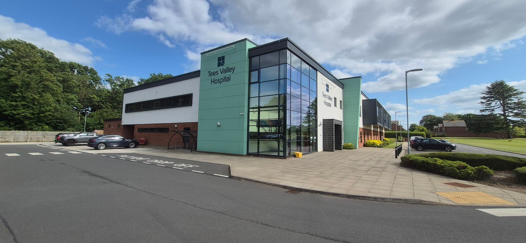 Modern building with large glass windows, "Tees Valley Hospital" sign, and landscaped surroundings in Tees Valley, Yorkshire.