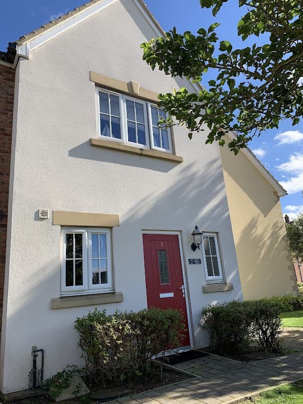 A charming two-story house with a red door, white walls, and a green garden in The Bay, Filey, Yorkshire.