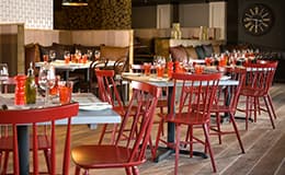 Elegant restaurant interior with red chairs, set tables, wooden floors, and cozy booth seating against patterned walls.