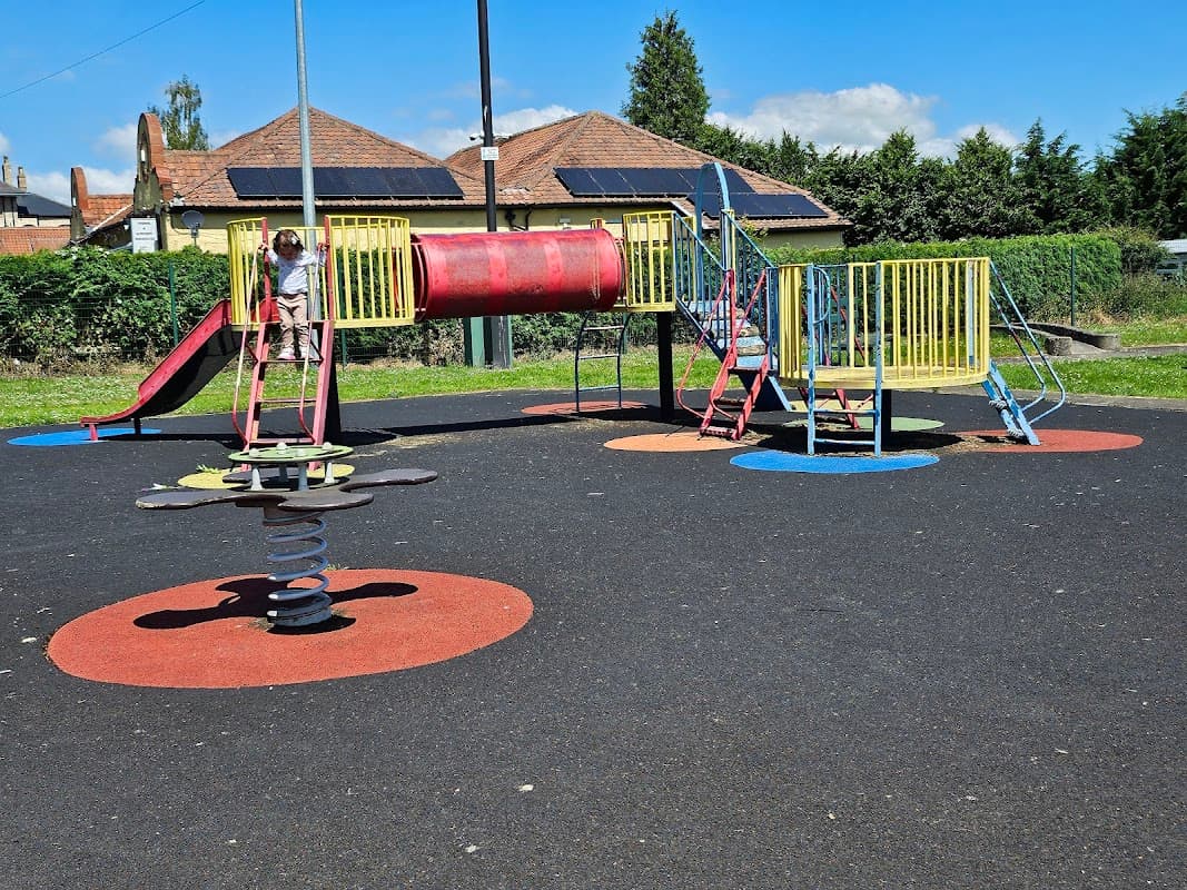 Colorful playground equipment with a slide, tunnel, and spring rider on a rubber surface under a clear blue sky.