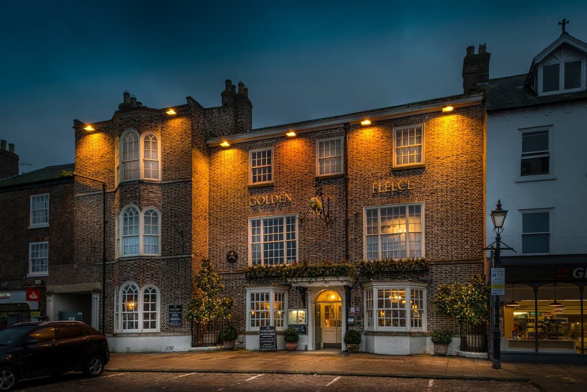 Historic brick building with illuminated windows, "Golden Fleece" signage, and a charming entrance in Thirsk, Yorkshire.