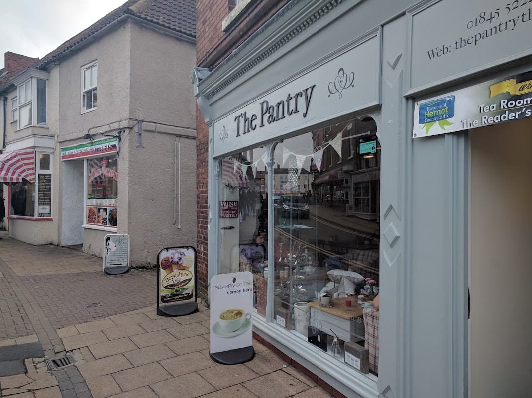 Quaint shopfront of "The Pantry" with decorative bunting, showcasing a variety of baked goods and a cozy atmosphere.