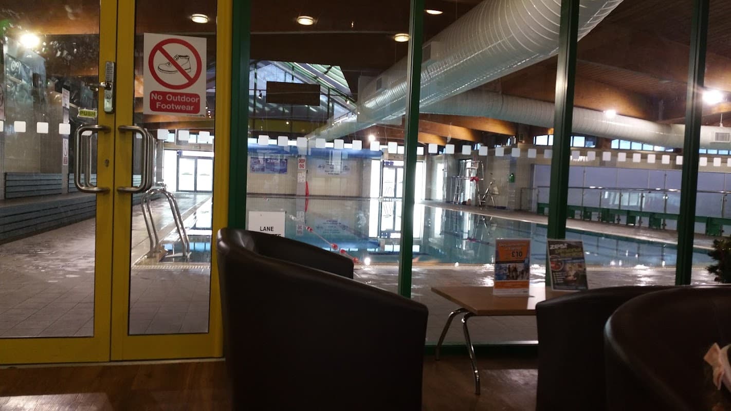 Indoor swimming pool visible through large glass doors, with seating area and signage about footwear policy.