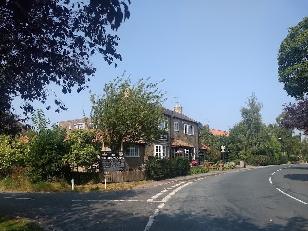 Country Living Adult Only Campsite with lush greenery, a quaint building, and a peaceful road in Thorganby, North Yorkshire.