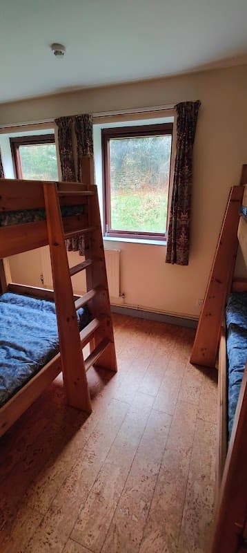 Wooden bunk beds in a cozy room with large windows overlooking greenery and patterned curtains.