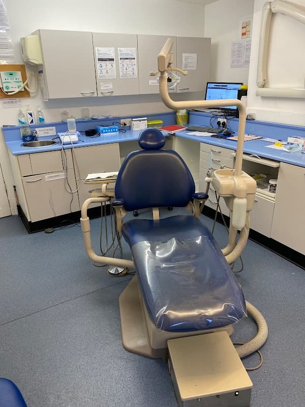 Dental chair in a clean clinic with cabinets, equipment, and a computer workstation in a well-lit room.