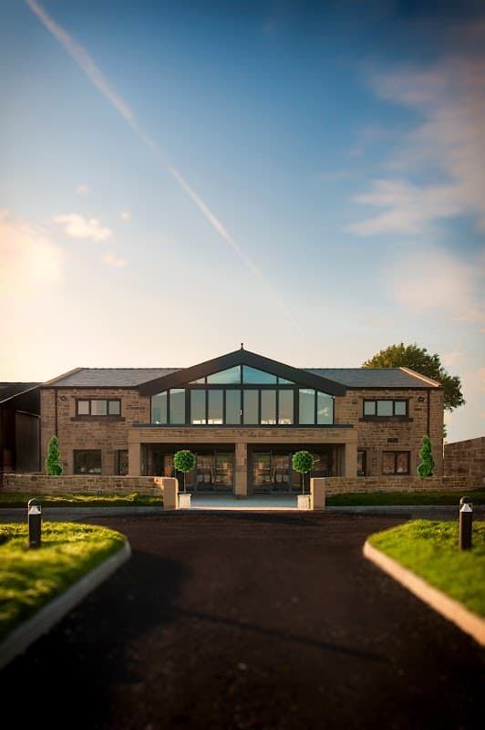 Modern stone building with large glass windows, flanked by manicured greenery and a clear blue sky.