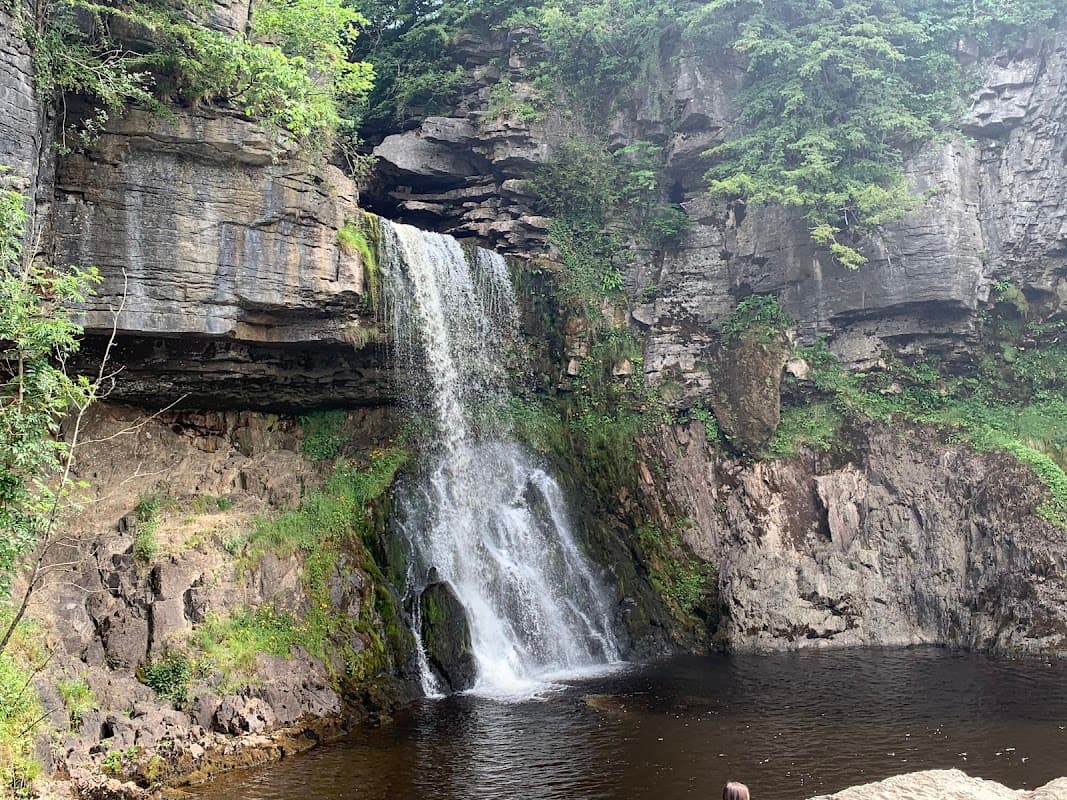 A picturesque waterfall cascading over rocky cliffs into a tranquil pool, surrounded by lush greenery.