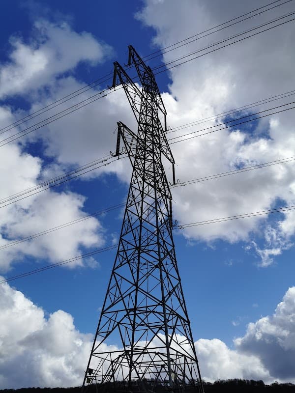 A tall power line tower against a backdrop of blue sky and fluffy white clouds.