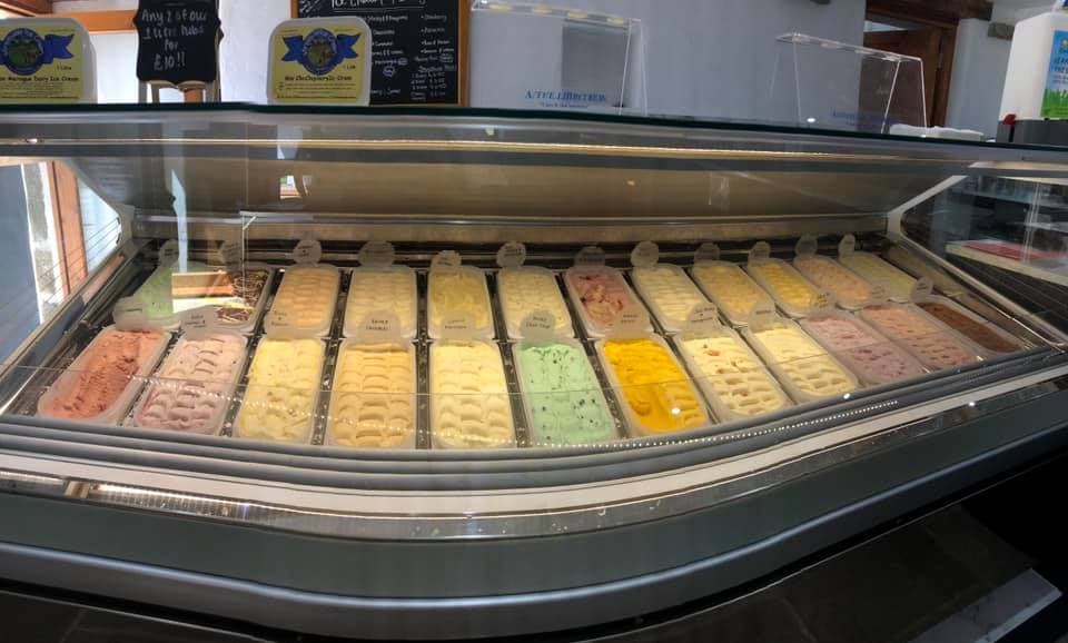 Colorful ice cream tubs displayed in a glass case at Wensleydale Ice Cream Parlour, with a menu board in the background.