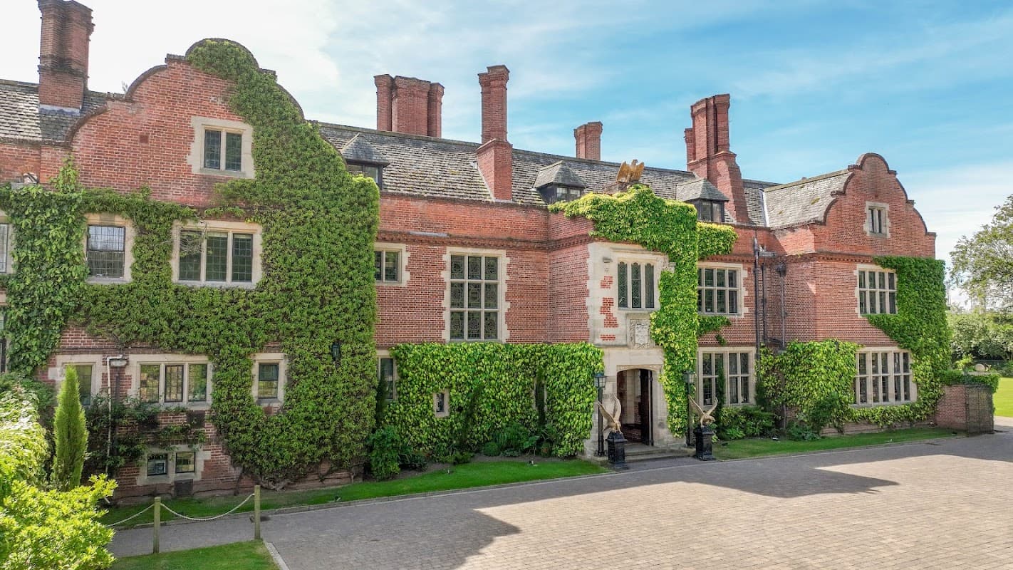 Historic brick building covered in greenery, featuring large windows and a grand entrance, set in a landscaped area.