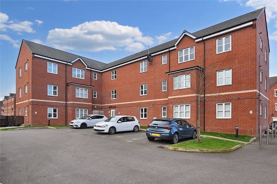 Residential car park featuring multiple parked cars and modern brick buildings under a blue sky in Tingley, Yorkshire.
