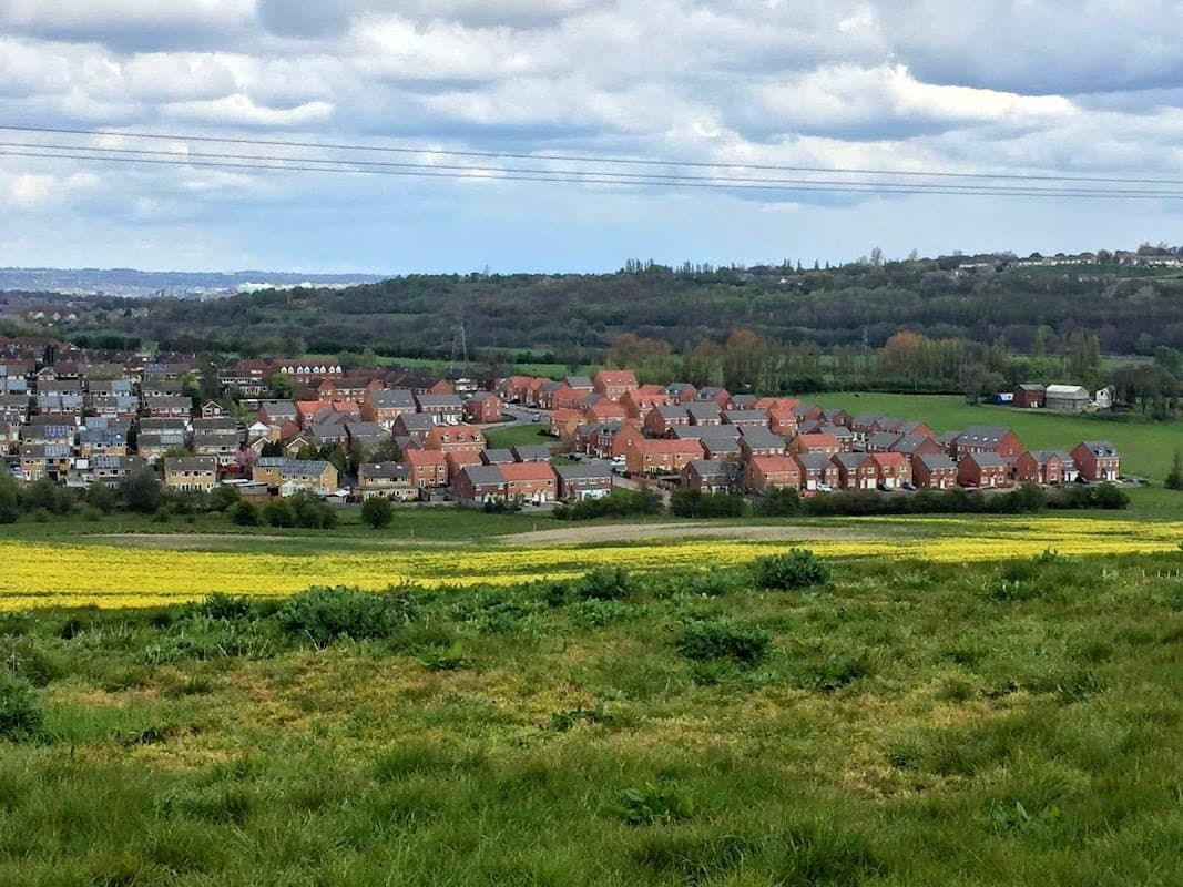 View of Topcliffe Grange Farm amidst green fields and residential homes under a cloudy sky in Tingley, Yorkshire.