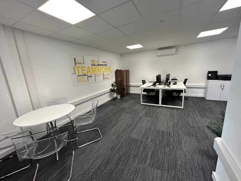 Modern office space featuring a white desk, chairs, a round table, and a wall mural emphasizing teamwork.