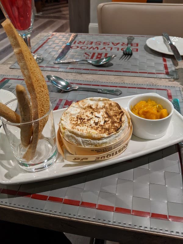 A plate featuring baked cheese, mango chutney, and breadsticks, set on a stylish table at Bollywood Brasserie.