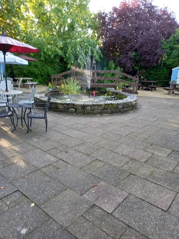 A courtyard with a stone fountain surrounded by greenery, picnic tables, and patio seating under umbrellas.