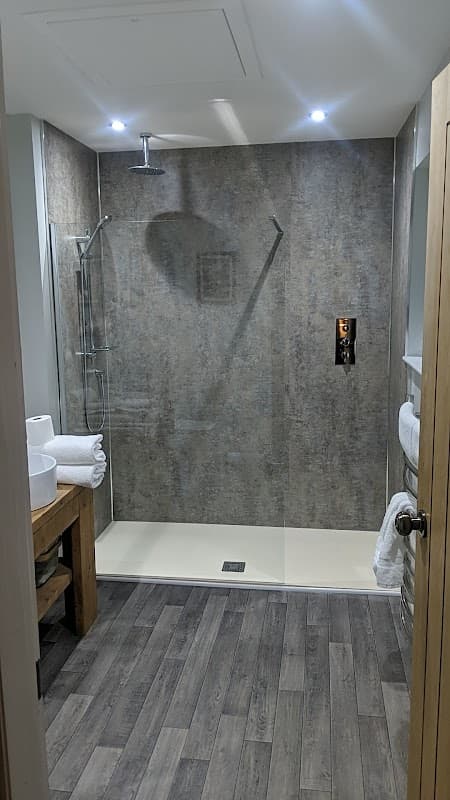Modern bathroom featuring a spacious walk-in shower, wooden accents, and neatly arranged towels on a shelf.