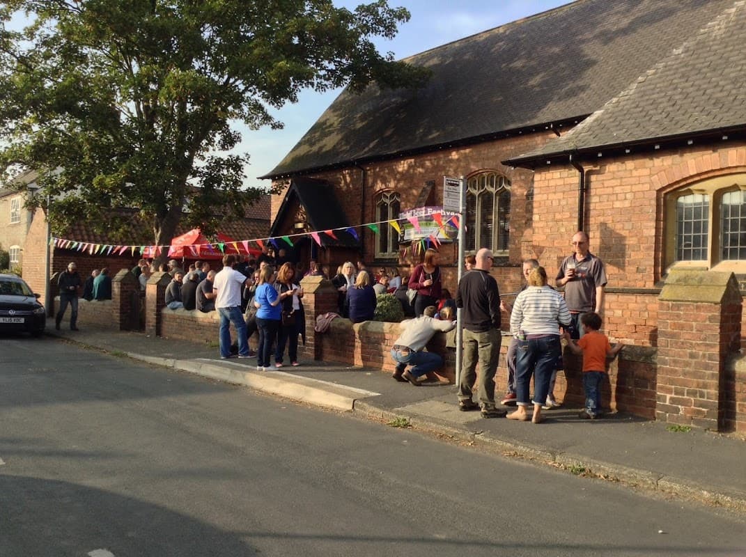 People gather outside Ulleskelf Village Hall, decorated with colorful bunting, enjoying a community event on a sunny day.