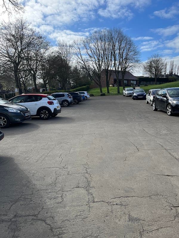 Free parking area in Wakefield, Yorkshire, with several parked cars and trees under a partly cloudy sky.