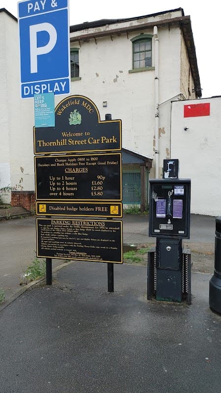 Sign for Thornhill Street Car Park with parking charges, payment machine, and nearby buildings in Wakefield, Yorkshire.