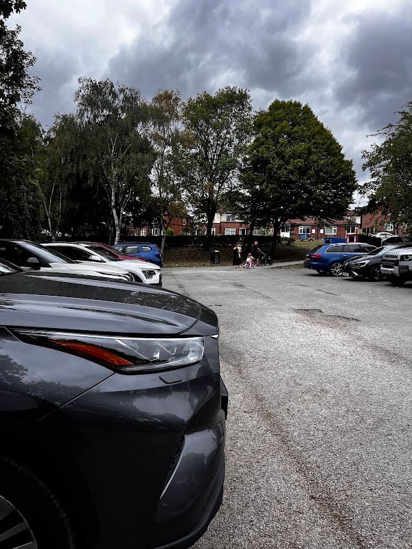 Car park with parked cars, trees in the background, and a cloudy sky over Wrenthorpe Park in Wakefield, Yorkshire.