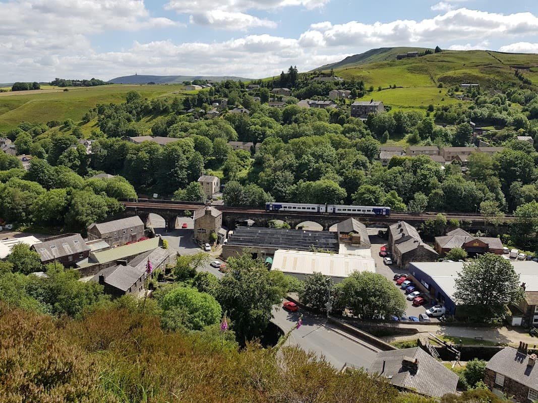 A scenic view of Walsden, Yorkshire, featuring green hills, a railway bridge, and quaint buildings nestled among trees.