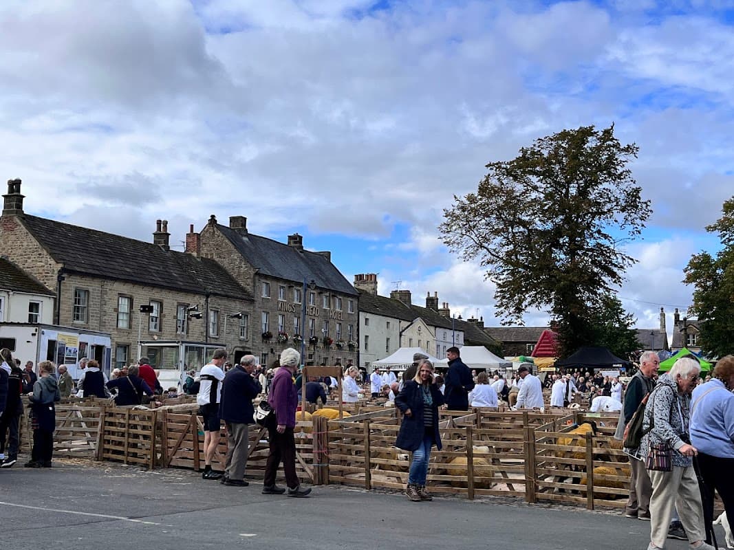 Busy marketplace in Warthermarske, Yorkshire, with vendors, livestock pens, and people interacting under a cloudy sky.