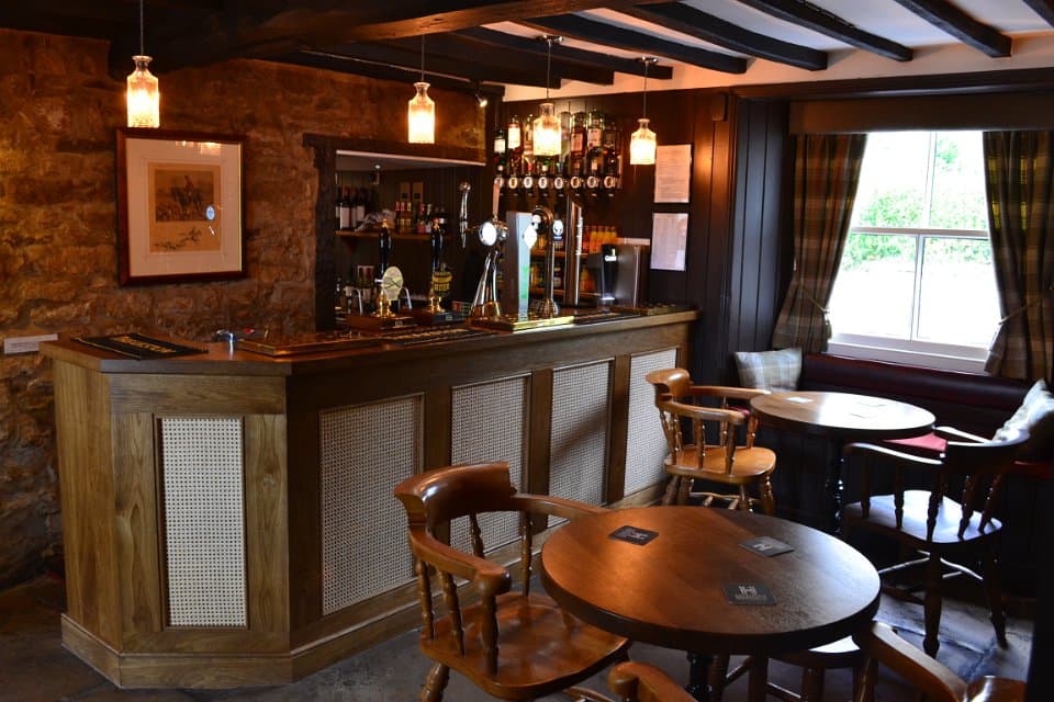 Cozy bar interior with wooden furniture, a stone wall, and shelves lined with various spirits and drinks.