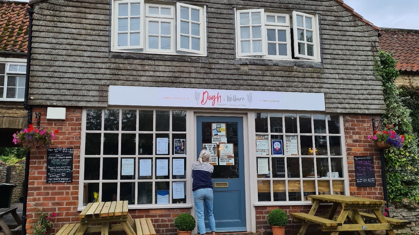 Charming grocery store with a wooden sign, flower baskets, and outdoor seating in Welburn, Yorkshire.