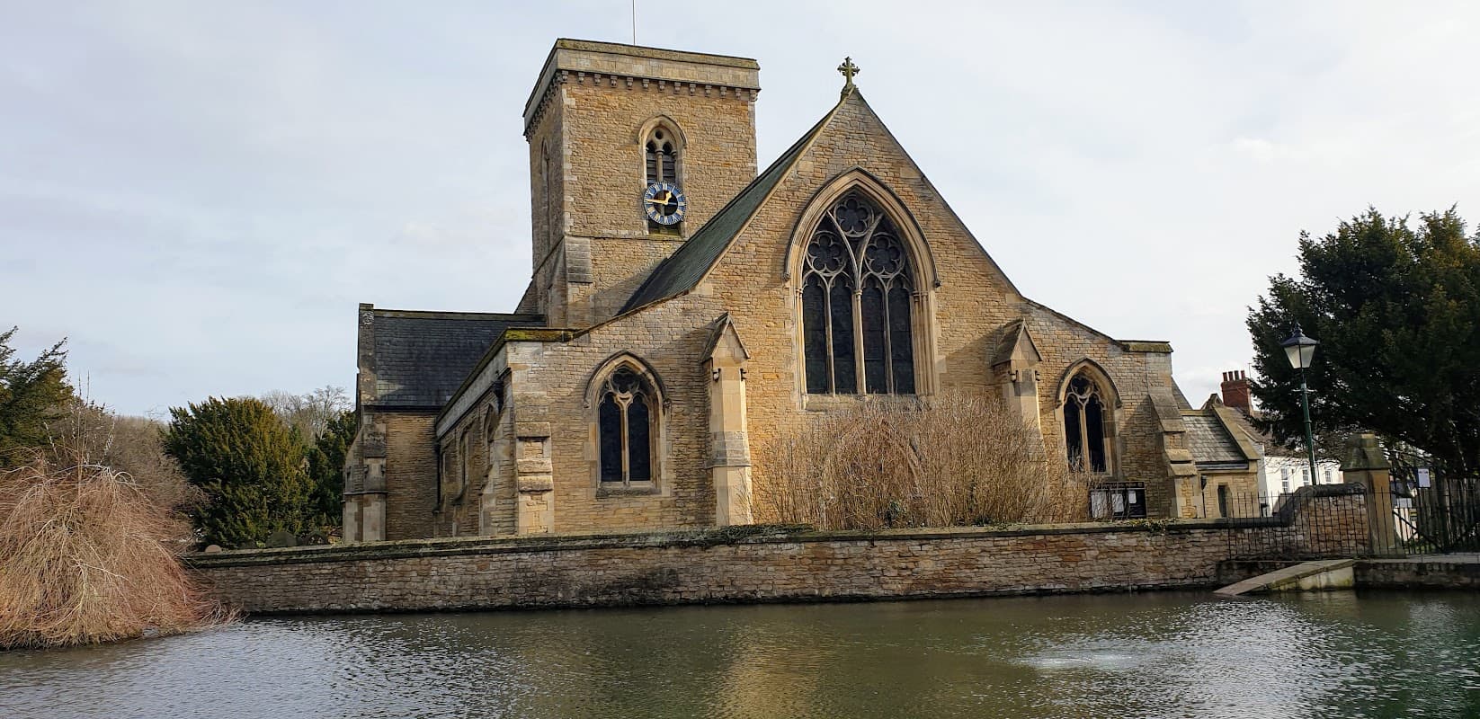 Welton Church with a stone faΓ§ade, tall tower, and surrounding water and trees in Welton, Yorkshire.
