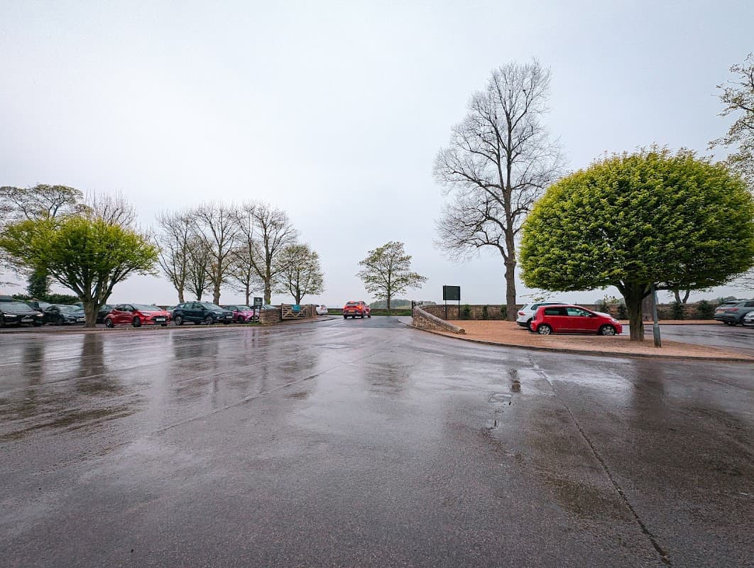 Car park with wet pavement, lined with trees, and parked cars under a cloudy sky in Wentworth, Yorkshire.