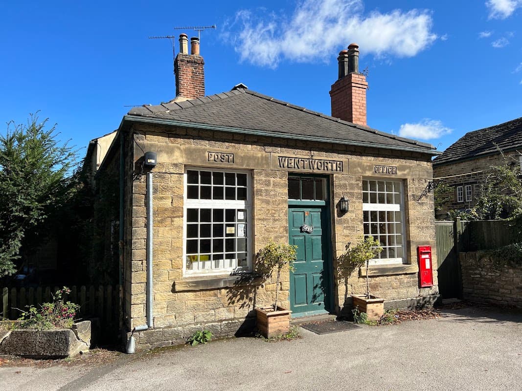Stone building with a green door, large windows, a red post box, and chimney stacks under a blue sky.