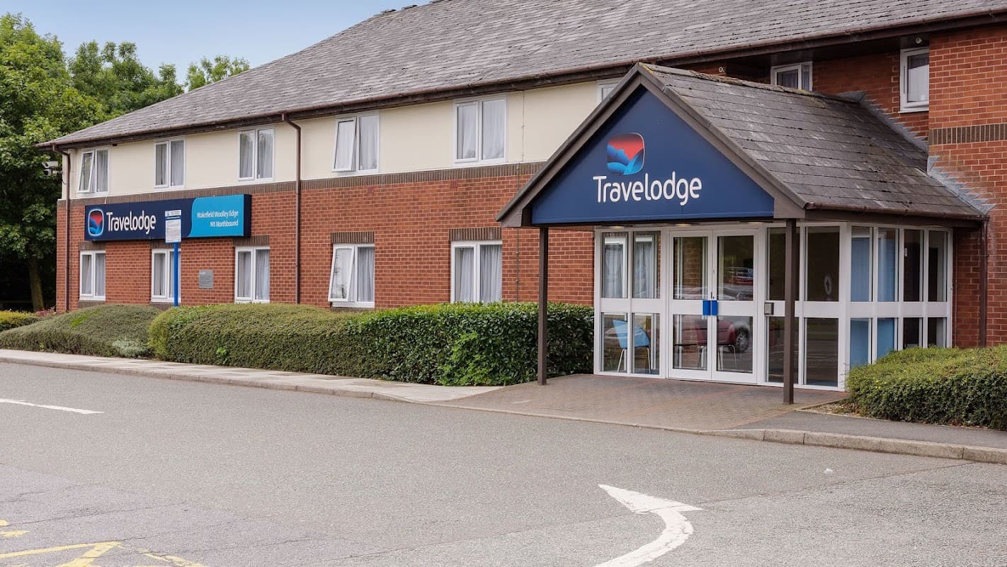 Travelodge hotel exterior with a blue sign, entrance canopy, and landscaped greenery in West Bretton, Yorkshire.
