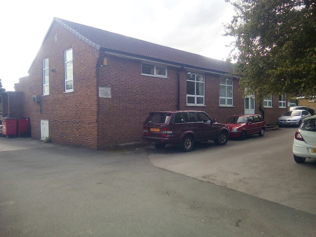 West Bretton Village Hall, a brick building with windows, surrounded by parked cars and greenery.