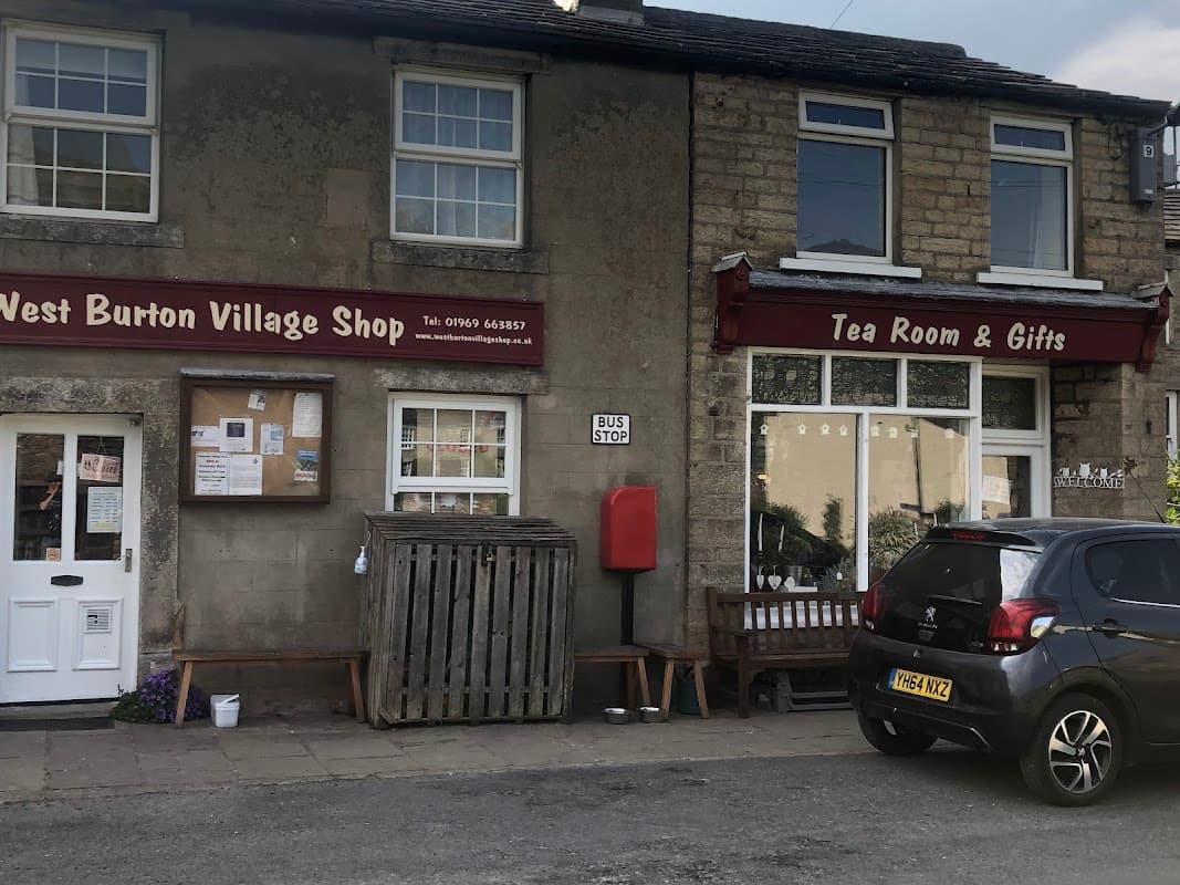West Burton Village Shop and Tea Room with a bus stop, wooden bench, and parked car outside a stone building.