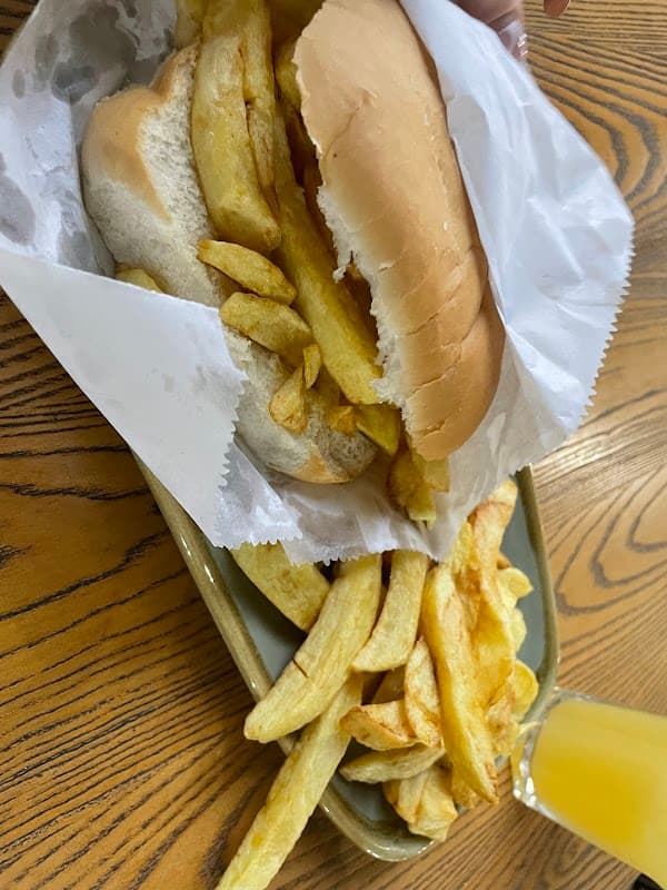 A tray with a sandwich filled with chips and a side of golden fries, accompanied by a glass of orange drink.