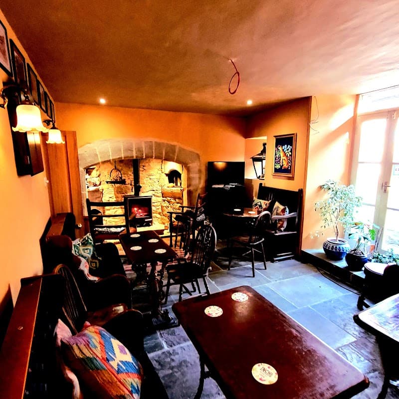 Cozy interior of The Fox & Hounds Inn, featuring a stone fireplace, wooden furniture, and warm orange walls.