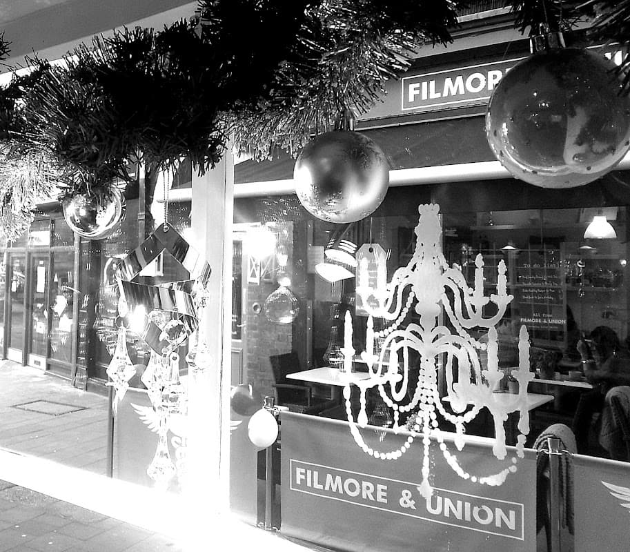 Decorative storefront with festive ornaments, a chandelier design, and reflections of a nearby restaurant in Wetherby.