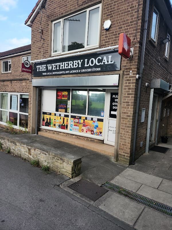 Corner shop with a sign reading "The Wetherby Local," displaying groceries and drinks, in a brick building.