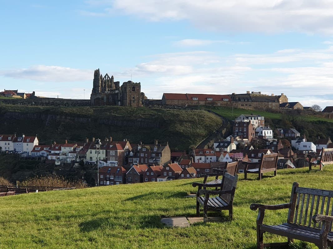 View of Whitby with benches in foreground, showcasing rooftops and the historic abbey on the cliff.