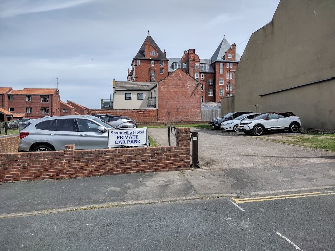 Saxonville Hotel car park with several parked cars and a sign reading "PRIVATE CAR PARK" against a backdrop of buildings.